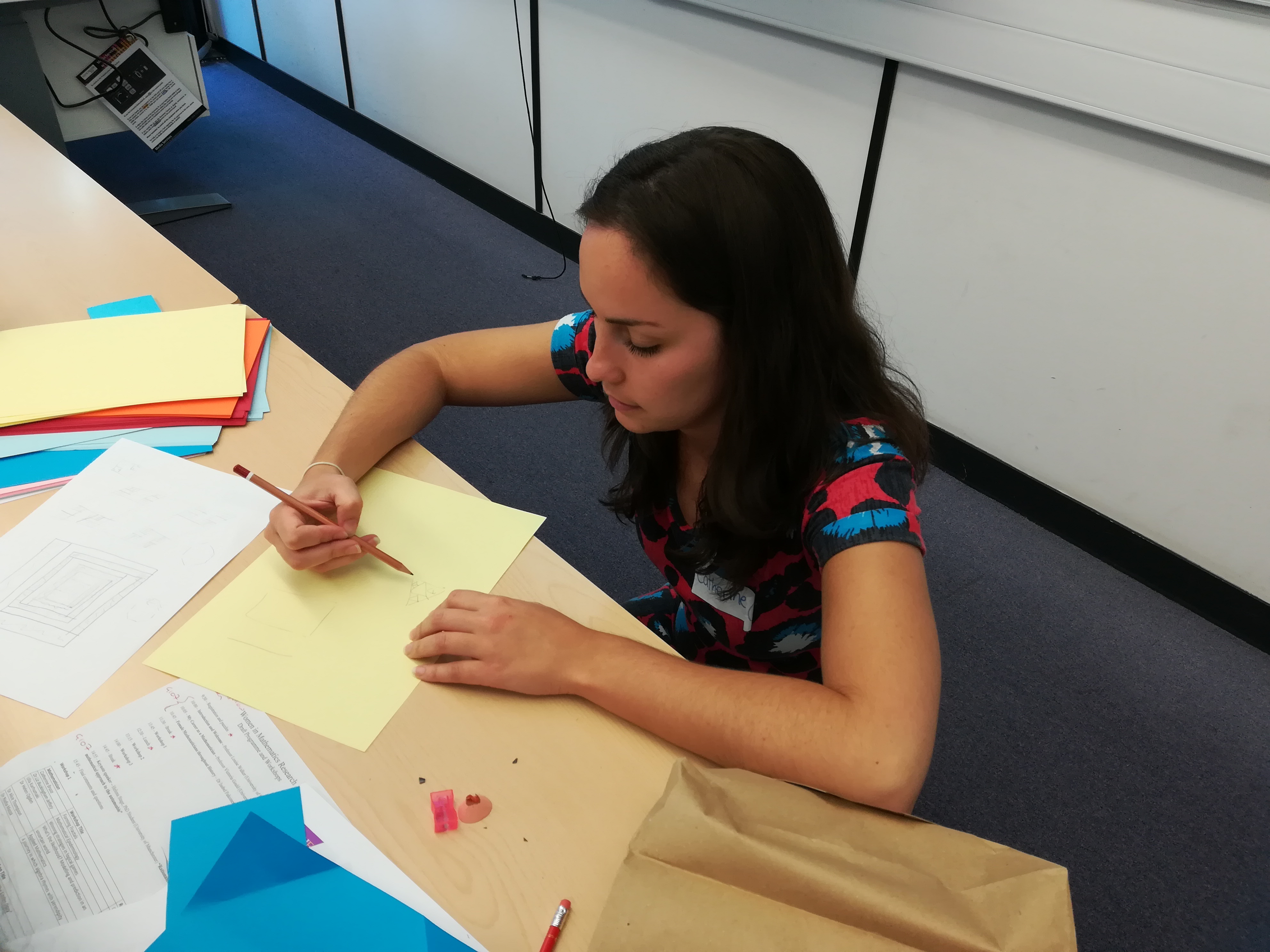 A photo of Catherine Bruce crouching at a table, drawing on a piece of paper
