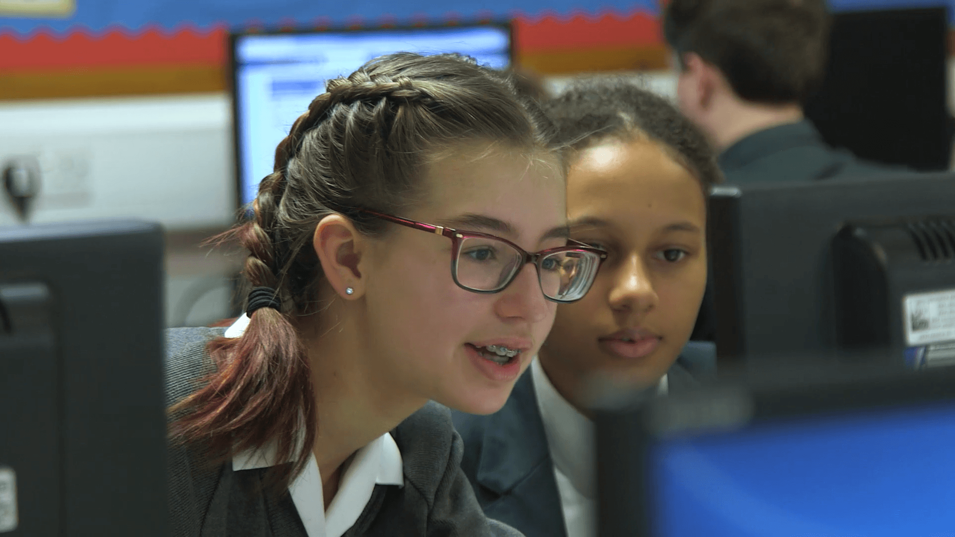 Photograph of two schoolgirls in a computer lab, reading a computer screen