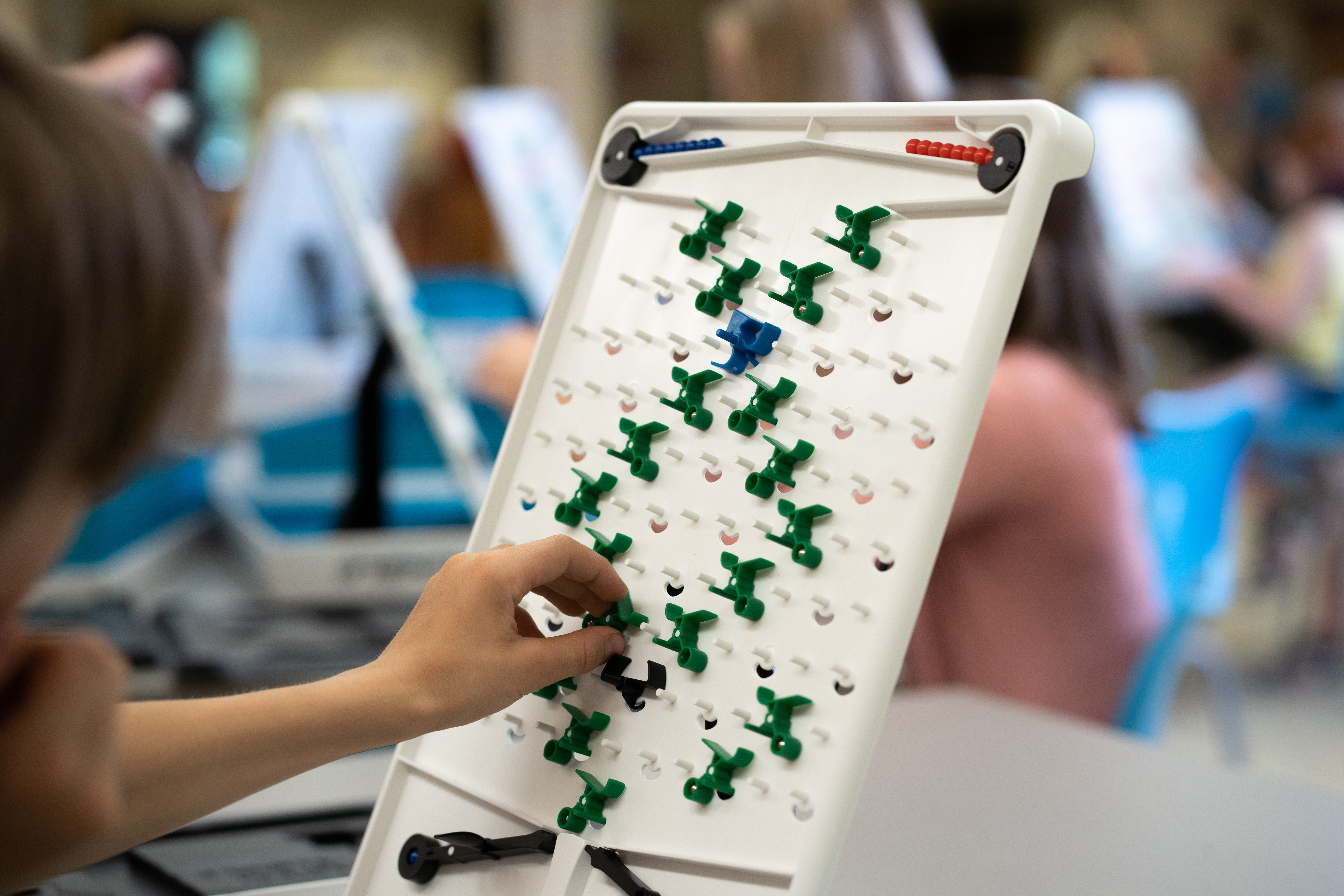 Photo of a Turing Tumble board with green pieces attached to pegs down the board, and marbles at the top